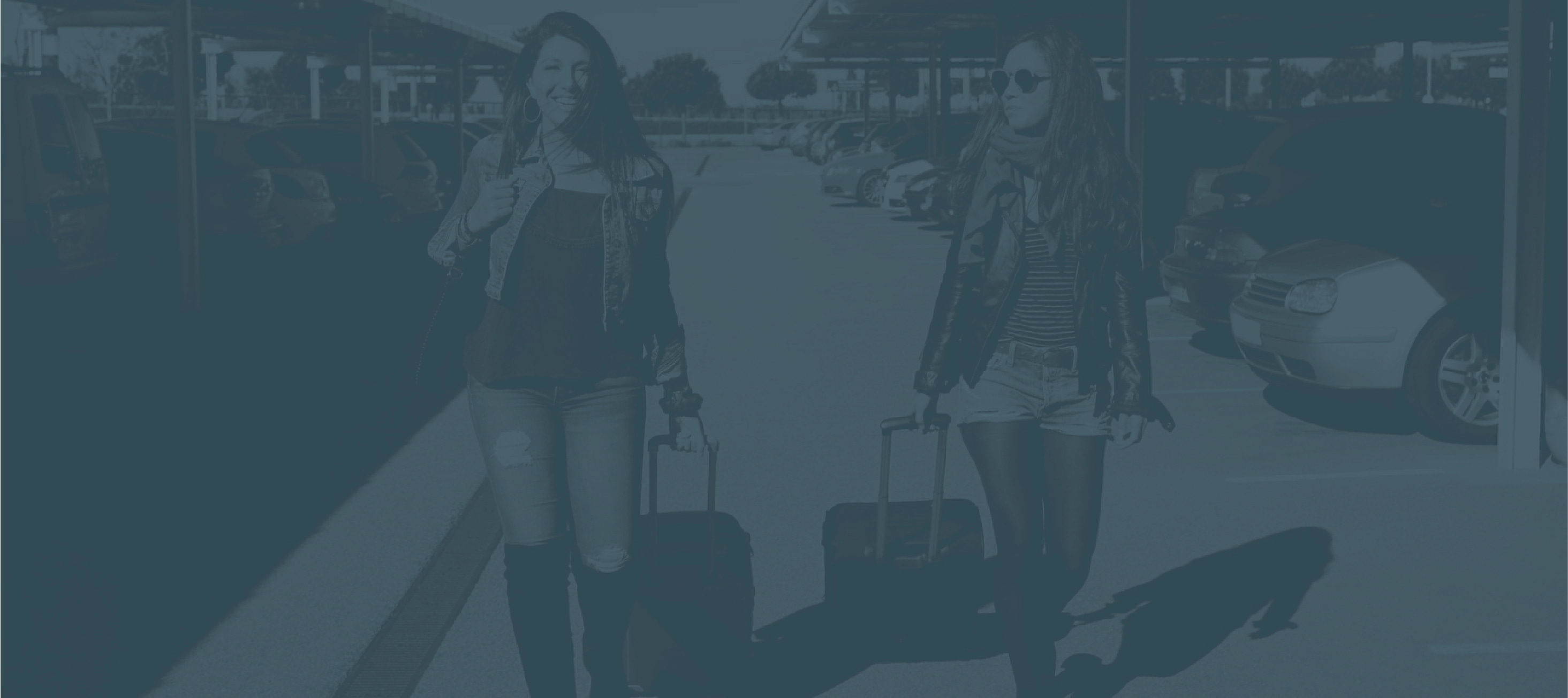 Two travelers with rolling suitcases outside an airport terminal